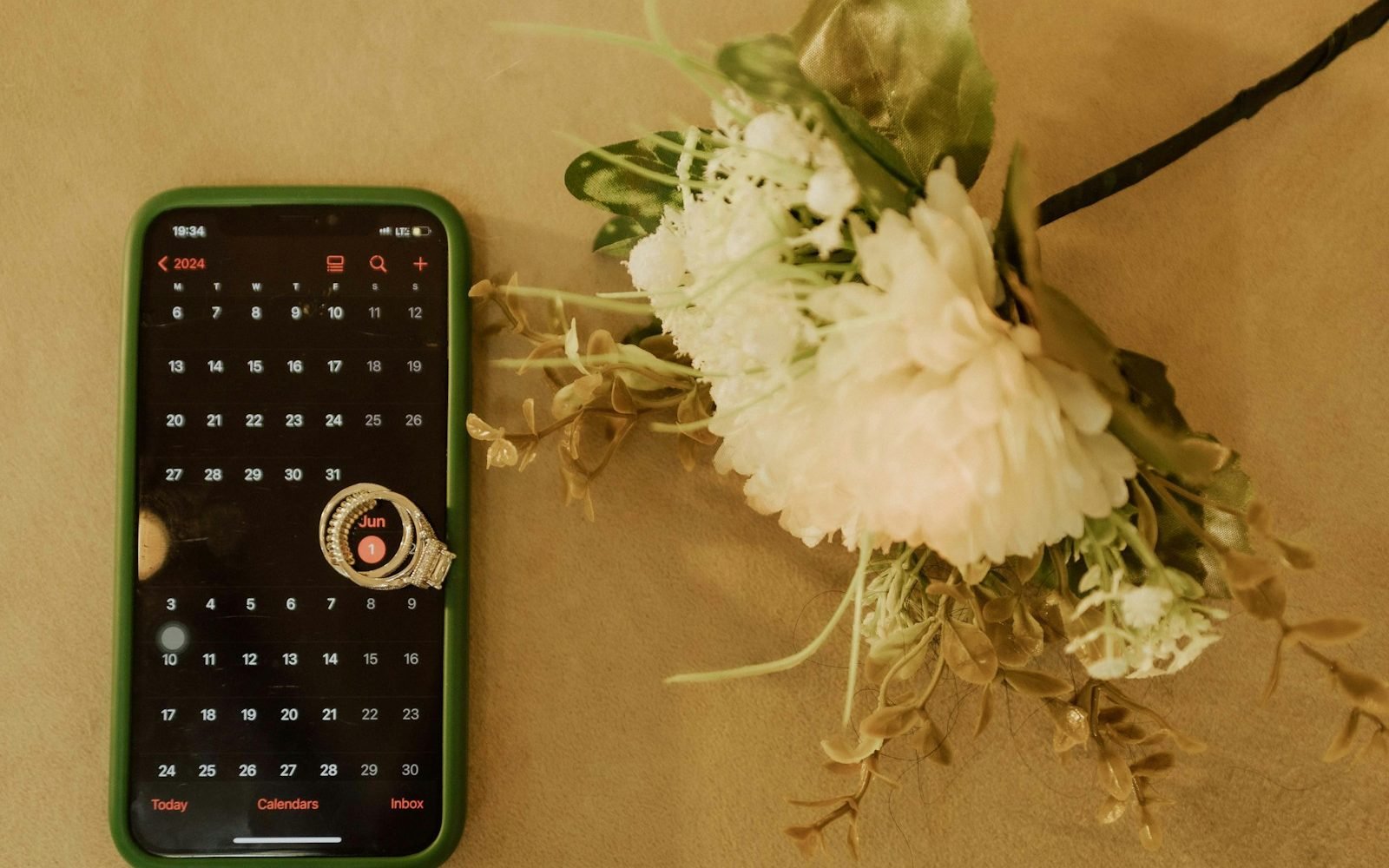 Teléfono con el calendario abierto junto a un ramo de flores blancas y un anillo. Foto: McFollis, Unsplash