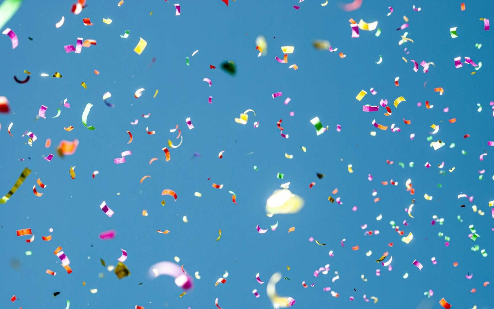 Confeti de colores cayendo contra un cielo azul despejado. Foto: Damiano Lingauri, Unsplash